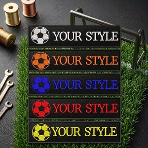 May include: A collection of embroidered patches with soccer ball designs in white, orange, blue, red, and yellow. Each patch has the text "YOUR STYLE" in a matching color. The patches are displayed on a black background with artificial grass.