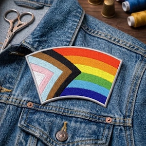 May include: A colorful embroidered patch featuring a rainbow design with additional stripes representing inclusivity. The patch is sewn onto a denim jacket, showcasing its potential use as an accessory. The patch is a vibrant mix of colors, including red, orange, yellow, green, blue, and purple.