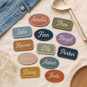 May include: A collection of embroidered name patches in various shapes and colors, featuring the names Amelia, Theo, Isla, Finn, Hazel, Rowan, Lily, Parker, Emma, Asher, Daisy, and Jude in white cursive script on fabric backgrounds.