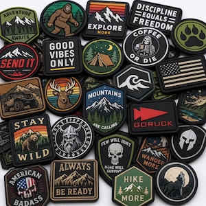 May include: A collection of various rubberized morale patches featuring diverse designs including mountains, wildlife, skulls, and motivational text such as "Stay Wild," "Explore More," and "Discipline Equals Freedom" in assorted shapes and colors.