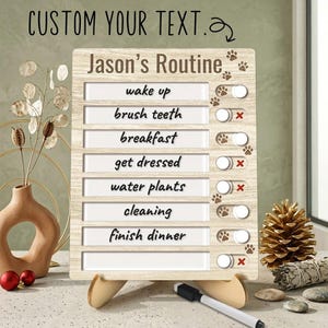 May include: A light wood-grain routine checklist board with the text Jason's Routine and a list of tasks including wake up, brush teeth, breakfast, get dressed, water plants, cleaning, and finish dinner, featuring sliding toggles with paw print icons.