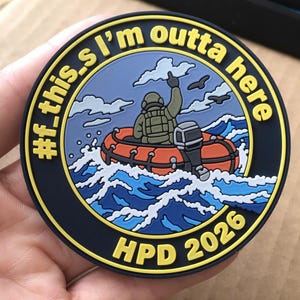 May include: A circular morale patch featuring a cartoon figure in a tactical vest sitting in an orange inflatable boat on blue waves. The text reads #f_this.I'm outta here and HPD 2026 in yellow lettering against a dark blue background.