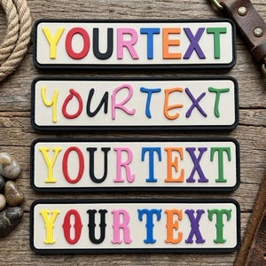 May include: Four rectangular patches with a white background and black border, each featuring the word YOURTEXT in raised, multi-colored letters. The letters are yellow, red, black, pink, blue, orange, purple, and green in various fonts.