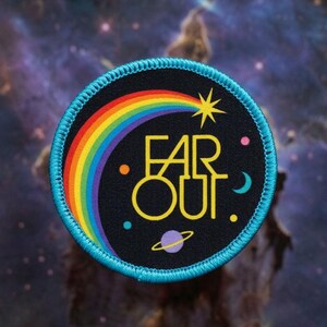 May include: A round, black patch with a rainbow, star, and planet design. The patch has the words "FAR OUT" in yellow. The patch is bordered with a light blue stitching. The background is a nebula.