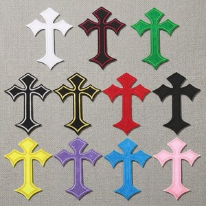 May include: A collection of eleven embroidered cross patches in various colors, including white, black, red, green, yellow, purple, blue, and pink. Each cross has a decorative border and is displayed on a neutral fabric background.