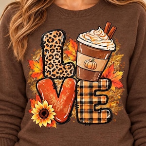 Puede incluir: Una sudadera marrón de cuello redondo con un gráfico que forma la palabra LOVE. La L tiene estampado de leopardo, la O es una taza de café con nata y canela, la V tiene un girasol y la E presenta un patrón de cuadros negros y naranjas.