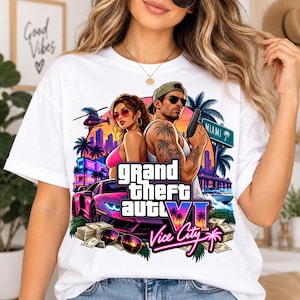 May include: A white t-shirt featuring a graphic print of a man and a woman standing back-to-back, a purple sports car, stacks of cash, a helicopter, palm trees, and a Miami street sign, with the text Grand Theft Auto VI Vice City.