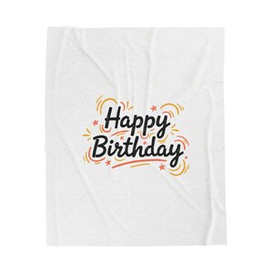 May include: White blanket with the words "Happy Birthday" in black script, accented with orange and red starbursts and stars. The blanket has a subtle, textured pattern.