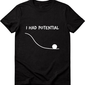 Pode incluir: Camiseta preta com o texto branco "I HAD POTENTIAL" acima de um desenho de linha branca de uma bola rolando por um caminho curvo. O gráfico é uma interpretação humorística da energia potencial.