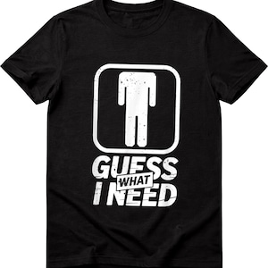 May include: Black t-shirt with a white graphic of a stick figure inside a square, with the words "GUESS WHAT I NEED" printed below. The design has a distressed, vintage look.