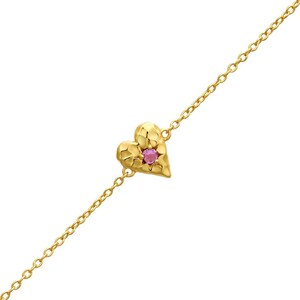 Könnte beinhalten: Ein Goldkettenarmband mit einem einzelnen herzförmigen Anhänger mit strukturierter, gehämmerter Oberfläche. Ein kleiner, runder, rosa Edelstein ist in der Mitte des goldenen Herzens gefasst, das an einer zarten, dünnen Goldgliederkette befestigt ist.