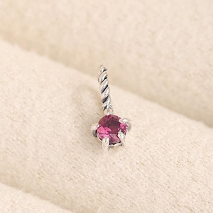 Könnte beinhalten: Ein silberner Ohrring mit einem gedrehten Stiel und einem magentafarbenen Edelstein. Der runde Edelstein ist in einer silbernen Fassung gefasst. Der Ohrring liegt auf einem weichen, cremefarbenen Hintergrund.