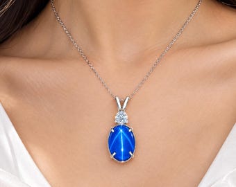 May include: A silver necklace featuring an oval-shaped blue star sapphire pendant with a prominent six-rayed star effect. The pendant is accented by a single round brilliant-cut white gemstone set above the sapphire, suspended on a delicate silver chain.