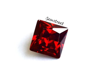 May include: A square-cut, faceted, deep red gemstone. The gem has sharp edges and a brilliant shine, reflecting light. The word "Gemstreet" is written in cursive on the top right corner. The gemstone is set against a white background.