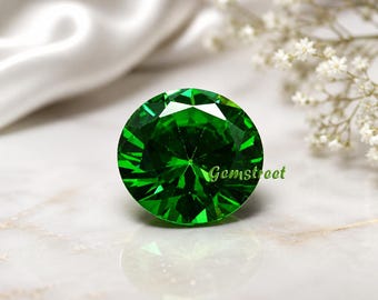 May include: A round, brilliant-cut vibrant green gemstone featuring multiple facets that reflect light. The word Gemstreet is printed in small green letters on the right side of the stone, which displays a clear reflection on the surface below.