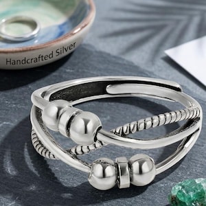 May include: A silver-toned adjustable ring featuring a multi-strand design with two smooth polished beads on one wire and two beads separated by a small rectangular spacer on another, accented by a twisted rope-textured wire element.