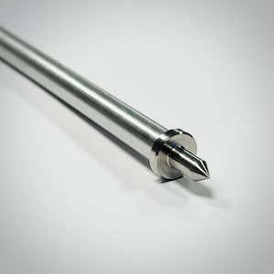 May include: A close-up of a silver metal tool with a pointed tip. The tool has a cylindrical body and a circular base near the tip. The background is a plain white surface.