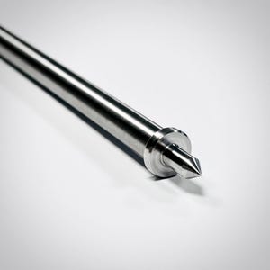May include: A silver-coloured metal rod featuring a smooth, cylindrical shaft that tapers to a sharp, pointed tip. The rod includes a circular collar or flange positioned just behind the conical point, creating a distinct transition in the metal form.