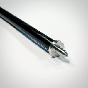 以下が含まれることがあります： 磨かれた銀色の金属製の先端を持つ、長く細い黒い棒。先端は鋭い円錐形に成形されており、平らな縁を持つ円形の金属製カラーに取り付けられています。このカラーは、滑らかで暗い円筒形のシャフトに直接接続されています。