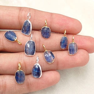 May include: A collection of nine small, faceted blue kyanite gemstone pendants. Each stone features a translucent, deep blue hue with natural internal variations and is encased in a thin metal bezel setting with a small circular jump ring bail.