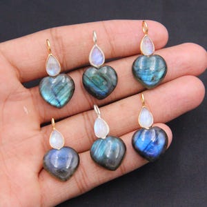 May include: Six heart-shaped labradorite pendants, each topped with a small, pear-shaped moonstone cabochon. The labradorite stones display iridescent blue flashes, while the moonstones have a milky white appearance. Each pendant has a metal bail.