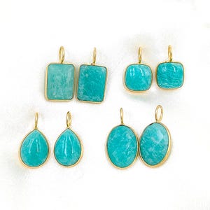 Puede incluir: Colección de seis pares de pendientes de piedras preciosas en varias formas: rectangular, cuadrada, de lágrima y ovalada. Cada pendiente presenta una piedra turquesa clara engastada en un marco de metal dorado. Sobre fondo blanco.