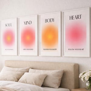 以下が含まれることがあります： グラデーションカラーのデザインとインスピレーションを与えるテキストが施された、額入りのウォールアートプリント4枚。「SOUL」、「MIND」、「BODY」、「HEART」とラベル付けされています。ニュートラルカラーの寝具と木製のナイトスタンドを備えたベッドの上に飾られています。
