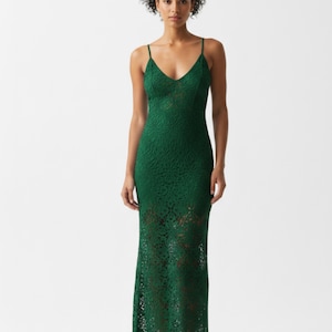 Può includere: Un abito lungo in pizzo verde smeraldo con scollo a V e spalline sottili. L'abito ha un corpetto aderente e una gonna fluida. L'intricato motivo in pizzo è visibile su tutto l'abito, creando un look delicato ed elegante.