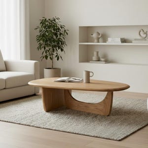Puede incluir: Un salón moderno con tonos neutros. Cuenta con un sofá de color claro, dos sillones, una mesa de centro de madera y una alfombra texturizada. Una planta en maceta y objetos decorativos completan la estética minimalista.