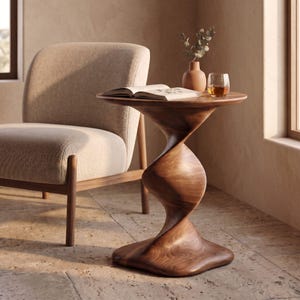 May include: A wooden side table with a spiralling, twisted pedestal base and a round top. On the table sits an open book, a small terracotta-coloured vase containing a sprig of greenery, and a clear glass tumbler filled with an amber liquid.