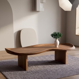 May include: A low-profile, kidney-shaped coffee table crafted from rich, dark brown wood with a smooth, curved surface and two sturdy slab legs. A small, white ceramic vase containing a lush green plant sits on the table's surface.