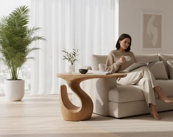 May include: A light-colored wooden side table with a curved, S-shaped base and a flat top surface. The table is positioned next to a beige sofa and a potted palm plant in a bright room with light-colored flooring and sheer white curtains.