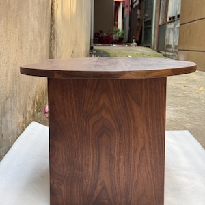 Pode incluir: Uma mesa de centro de perfil baixo feita de madeira de nogueira castanho-escura, com uma superf&iacute;cie de mesa oval e arredondada suave, e uma base vertical retangular s&oacute;lida que proporciona uma base resistente com um acabamento de veio natural.