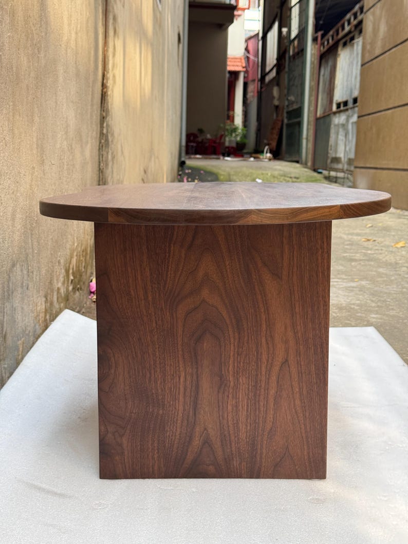 Pode incluir: Uma mesa de centro de perfil baixo feita de madeira de nogueira castanho-escura, com uma superf&iacute;cie de mesa oval e arredondada suave, e uma base vertical retangular s&oacute;lida que proporciona uma base resistente com um acabamento de veio natural.