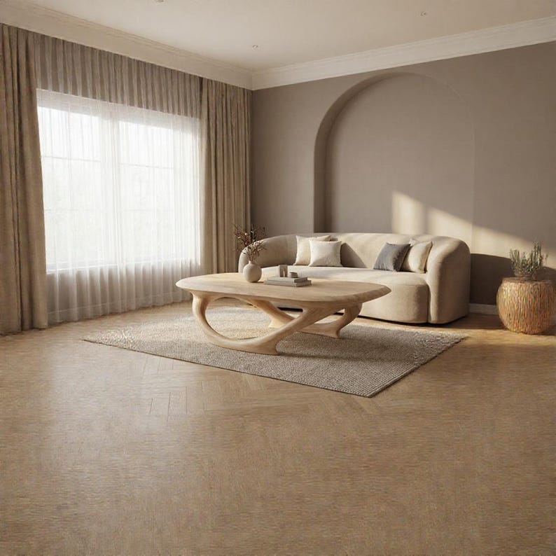 May include: A light-toned wooden coffee table with a curved, sculptural base sits in a room with a beige sofa, a textured area rug, and floor-to-ceiling curtains. The table features a smooth, oval-shaped top supported by an organic, flowing frame.