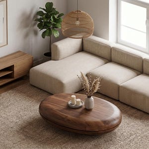 May include: A living room featuring a beige sectional sofa, a wooden media console, and an oval walnut coffee table. The table holds a small vase with dried stems and a plate with two white candles. A woven rug sits beneath the furniture.