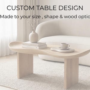 Pode incluir: Uma mesa de centro de madeira clara com um design curvo único. A mesa tem duas pernas retangulares e um tampo curvo. O texto "CUSTOM TABLE DESIGN" e "Made to your size, shape & wood options" é exibido acima da mesa.