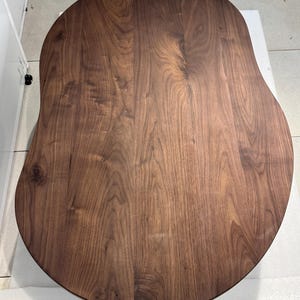 Pode incluir: Um tampo de mesa de madeira castanho-escura com um acabamento liso e polido e uma forma org&acirc;nica distinta de rim. A superf&iacute;cie apresenta um padr&atilde;o de gr&atilde;o de madeira natural proeminente com linhas onduladas e n&oacute;s vis&iacute;veis.