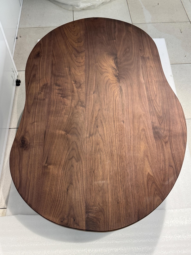 Pode incluir: Um tampo de mesa de madeira castanho-escura com um acabamento liso e polido e uma forma org&acirc;nica distinta de rim. A superf&iacute;cie apresenta um padr&atilde;o de gr&atilde;o de madeira natural proeminente com linhas onduladas e n&oacute;s vis&iacute;veis.