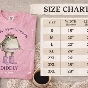 Puede incluir: Una camiseta rosa con el gr&aacute;fico de una rana que lleva sombrero, cintur&oacute;n y botas, junto al texto 'THE ONLY SQUAT I'M DOIN' IS DIDDLY'. Al lado hay una tabla de tallas que muestra anchos y largos en pulgadas para las tallas S a 3XL.
