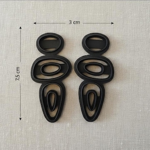 Peut inclure: Paire de boucles d'oreilles abstraites noires. Chaque boucle d'oreille mesure 7,5 cm de long et 3 cm de large. Les boucles d'oreilles ont un design ovale et en forme de goutte. Les boucles d'oreilles sont en matériau noir uni.