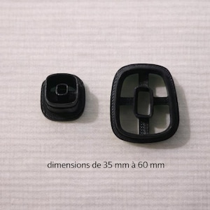 Peut inclure: Deux emporte-pièces en plastique noir. L'un est de petite forme carrée, l'autre est une conception plus grande et ouverte avec un centre carré. Le texte sur l'image indique "dimensions de 35 mm à 60 mm."