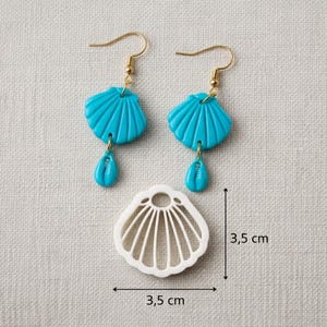 Könnte beinhalten: Türkisfarbene Muschelohrringe mit goldfarbenen Haken und einem passenden muschelförmigen Anhänger. Die Ohrringe haben einen tropfenförmigen Anhänger. Der Anhänger und die Ohrringe sind jeweils 3,5 cm groß.