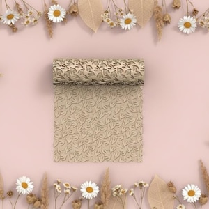 May include: A beige, leaf-patterned rolling pin with a matching sheet of embossed material. The rolling pin is rolled out, revealing the pattern. The background is a soft pink, decorated with flowers and leaves.