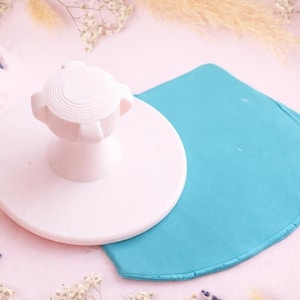 Peut inclure: Un outil de décoration de gâteau rose clair avec une poignée et un carré de fondant bleu clair. L'outil a une base circulaire et un dessus strié. Le fondant est d'une couleur bleu vif unie.