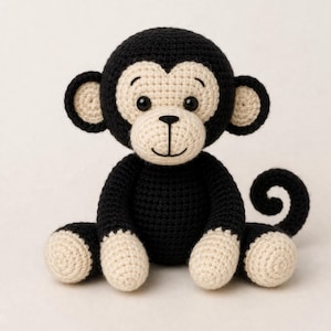 May include: A handmade crochet monkey in black and cream. The plush toy has a round head with large ears, a cream-colored face, and a smiling mouth. The monkey is sitting with its legs extended and a curled tail.