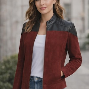 Könnte beinhalten: Burgunderfarbene Wildlederjacke mit schwarzen Lederakzenten an Schultern und Kragen. Die Jacke hat einen Reißverschluss und Taschen. Das Model trägt ein weißes Oberteil und blaue Jeans.