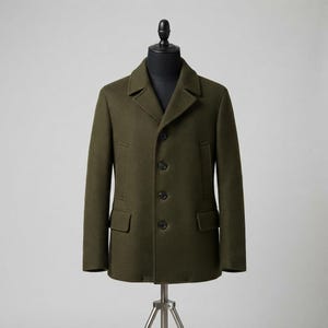 Könnte beinhalten: Ein olivgrüner Cabanjacke mit steigendem Revers, einer vier-Knopf-Vorderseite und zwei unteren Pattentaschen. Der Mantel wird auf einer Schneiderpuppe präsentiert und zeigt eine strukturierte Silhouette mit langen Ärmeln und einer glatten Oberfläche.