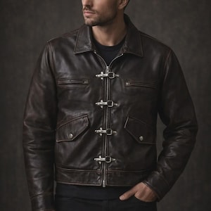 May include: A brown leather jacket with a collared neckline and silver-tone toggle closures. The jacket has two front pockets with flaps and a zipper closure. The model is wearing a black shirt and black pants.