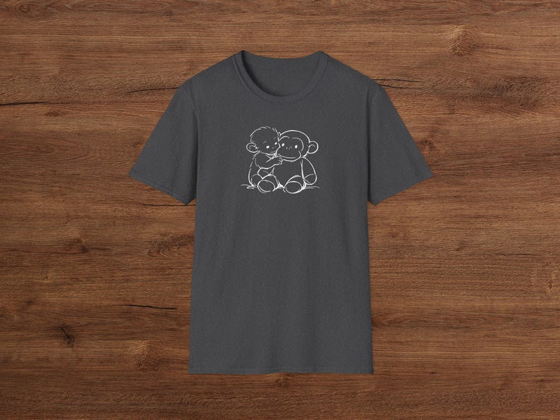 May include: Dark grey t-shirt with a white outline illustration of a child embracing a monkey. The design is positioned centrally on the chest. The shirt has short sleeves and a crew neck.
